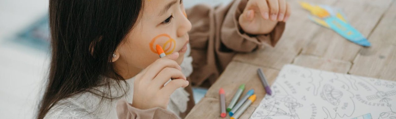 Young girl having fun with face painting and drawing, expressing creativity and joy.
